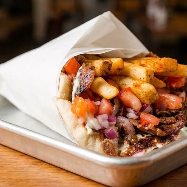 A gyros wrap filled with meat, fries, tomatoes, and onions, served on a metal tray.